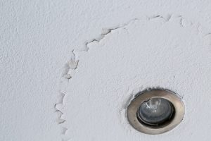 A cracked ceiling with peeling layer due to water leak. LED light.